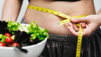 Woman measuring her waist while holding her healthy food.