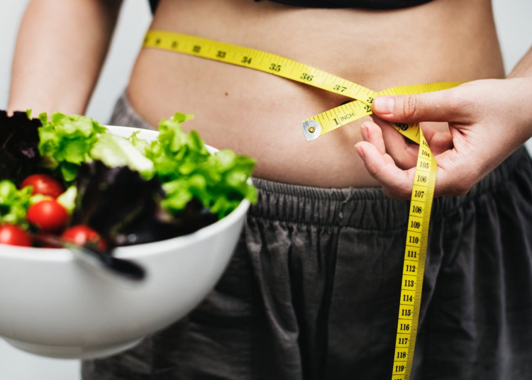 Woman measuring her waist while holding her healthy food.