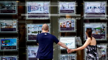 A couple view properties for sale in an estate agents window in London