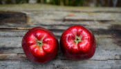 Two red apples on gray wooden surface.