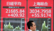 A man walks past an electric screen showing Japan's Nikkei and Shanghai Stock Exchange markets' indices outside a brokerage in Tokyo