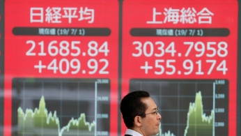 A man walks past an electric screen showing Japan's Nikkei and Shanghai Stock Exchange markets' indices outside a brokerage