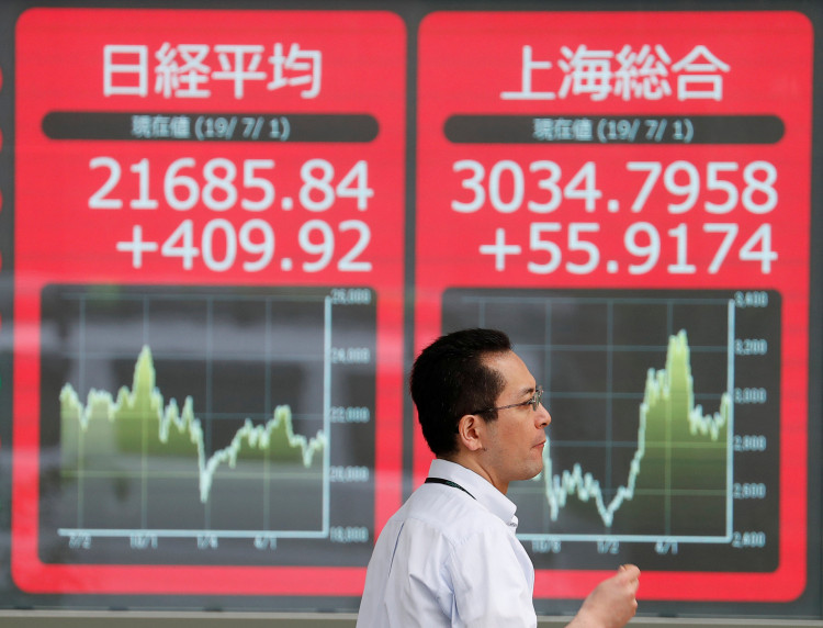 A man walks past an electric screen showing Japan's Nikkei and Shanghai Stock Exchange markets' indices outside a brokerage