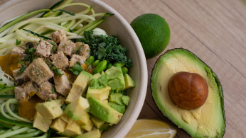 Bowl of salad with avocado on the side.