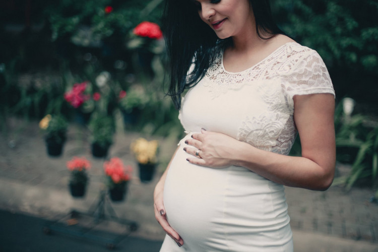 Close-up photo of pregnant woman in white dress.