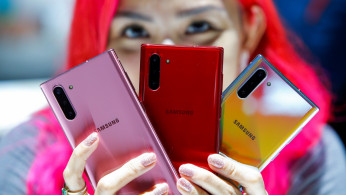 A woman holds different colored models of the Samsung Galaxy Note 10 while people test new devices during the launch event of the Galaxy Note 10 at the Barclays Center in Brooklyn