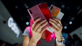 A woman holds different colored models of the Samsung Galaxy Note 10 while people test new devices during the launch event of the Galaxy Note 10 at the Barclays Center in Brooklyn