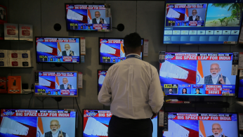 A salesman watches Prime Minister Narendra Modi addressing to the nation, on TV screens inside a showroom in Mumbai